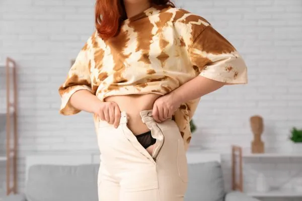 Image of woman trying to do her trousers up after pregnancy weight gain Wembley