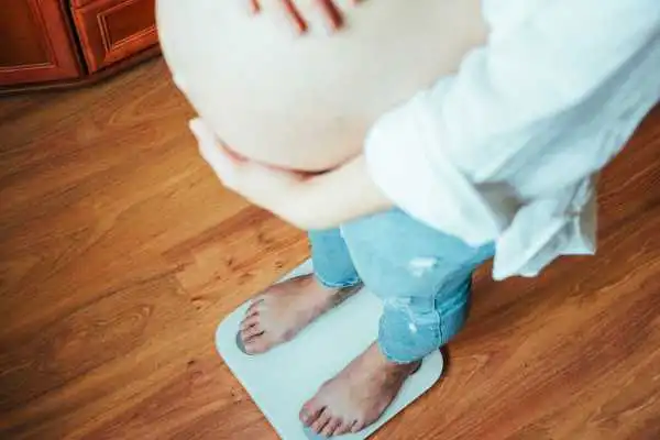 Image of woman weighing herself and experiencing weight gain through pregnancy Wembley